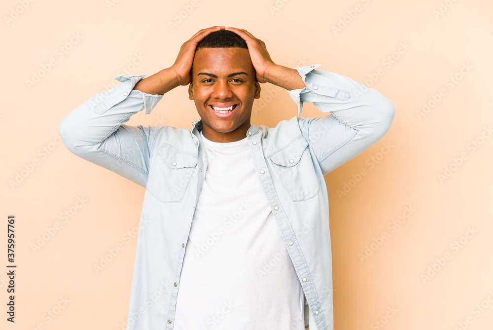 Young latin man isolated on beige background laughs joyfully keeping hands on head. Happiness concept.