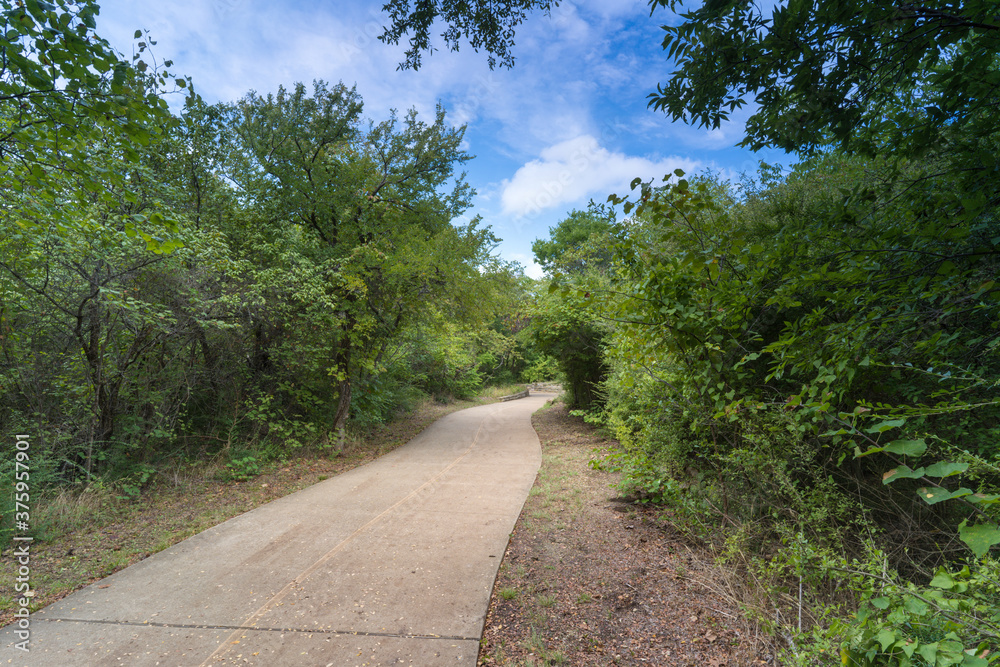 A concrete path in a Texas urban nature reserve on a sunny September day.