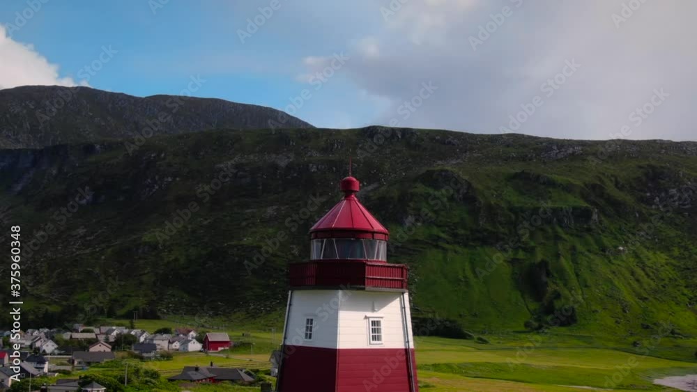 Aerial drone shot with vertigo effect (dolly zoom) of red-white lighthouse on the edge of Norway with the ocean and nice green fjords in the background.
