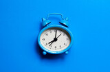 Alarm clock on a blue background top view flat lay with copy space. Minimalistic monochrome concept of time, deadline, work, morning.
