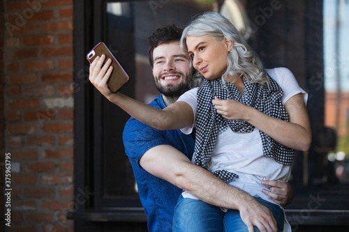 Young couple hanging out in front of cafe, using mobile phone to take a selfie 