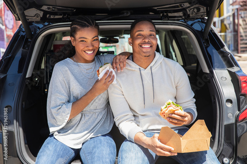 Portrait of young African American couple having impromptu picnic lunch in the back of their vehicle.