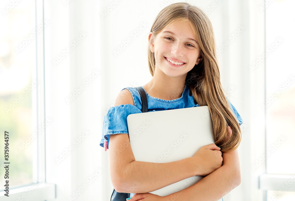 Joyful girl with backpack holding laptop on light background Joyful girl with backpack holding laptop on light background