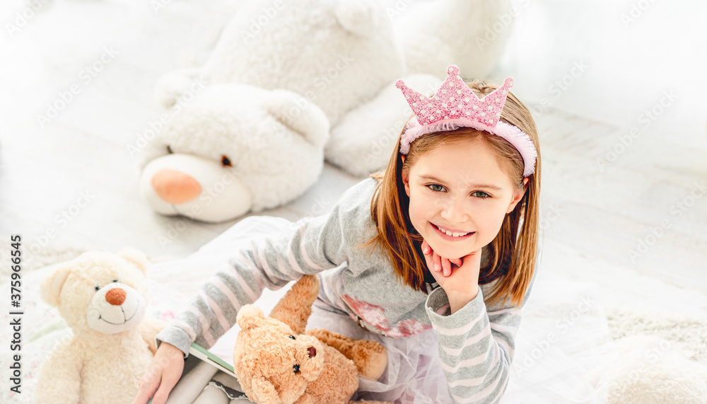 Fototapeta premium Adorable little girl in diadem with teddy bears in bright room
