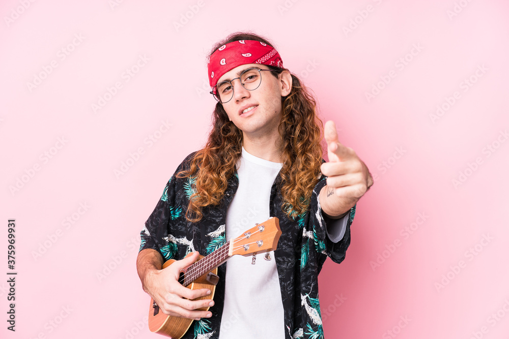 Long hair hippie man holding a ukelele isolated cheerful smiles pointing to front. Long hair hippie man holding a ukelele isolated cheerful smiles pointing to front.