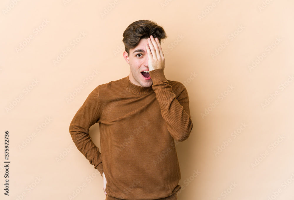 Young caucasian man isolated on beige background having fun covering half of face with palm. Young caucasian man isolated on beige background having fun covering half of face with palm.