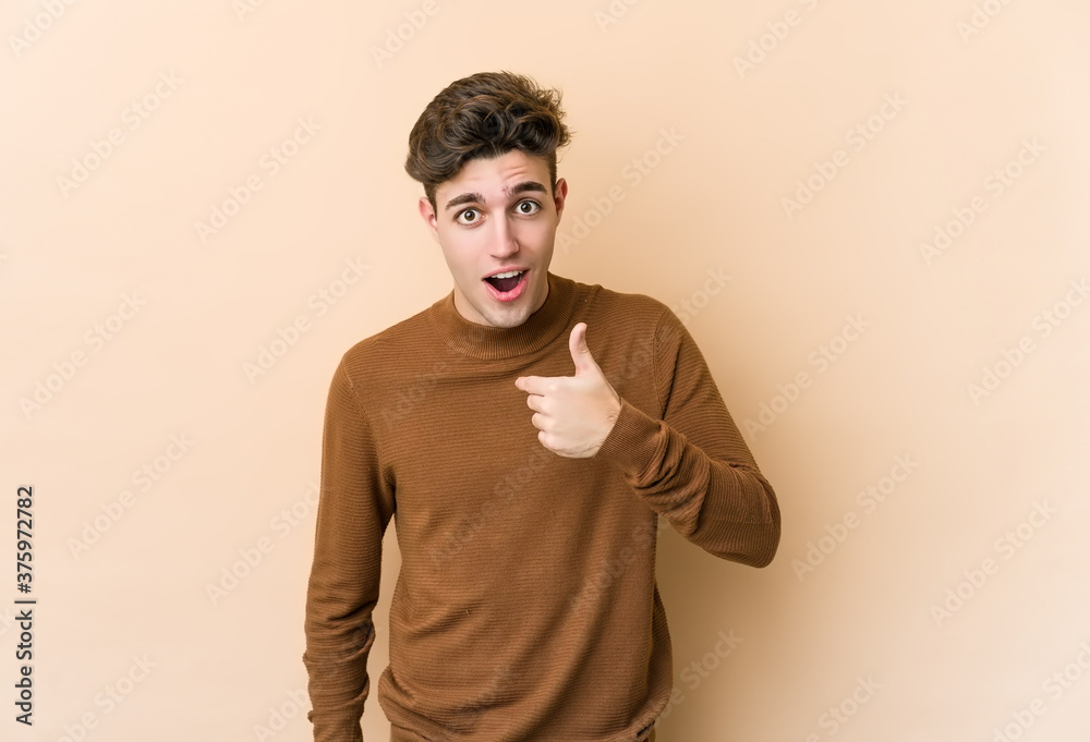 Young caucasian man isolated on beige background surprised pointing with finger, smiling broadly. Young caucasian man isolated on beige background surprised pointing with finger, smiling broadly.