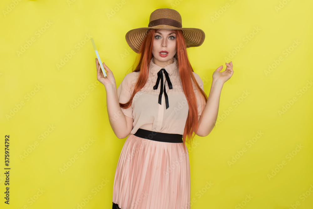 Red haired woman in straw hat over yellow background holding book in her hands Red haired woman in straw hat over yellow background holding book in her hands