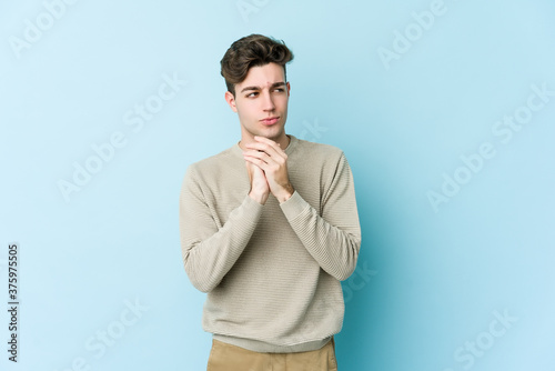 Young caucasian man isolated on blue background making up plan in mind, setting up an idea.