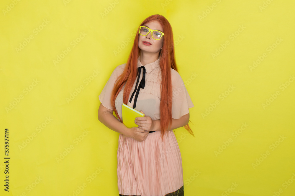 Red haired woman over yellow background holding book in her hands Red haired woman over yellow background holding book in her hands