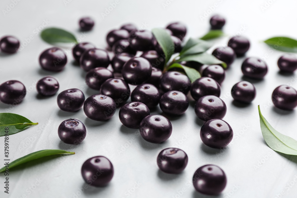 Fresh acai berries and green leaves on light grey table, closeup Fresh acai berries and green leaves on light grey table, closeup
