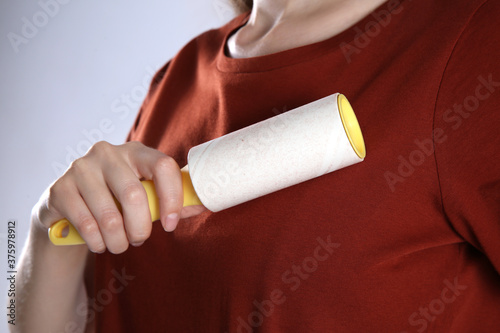 Woman cleaning red t-shirt with lint roller on grey background, closeup