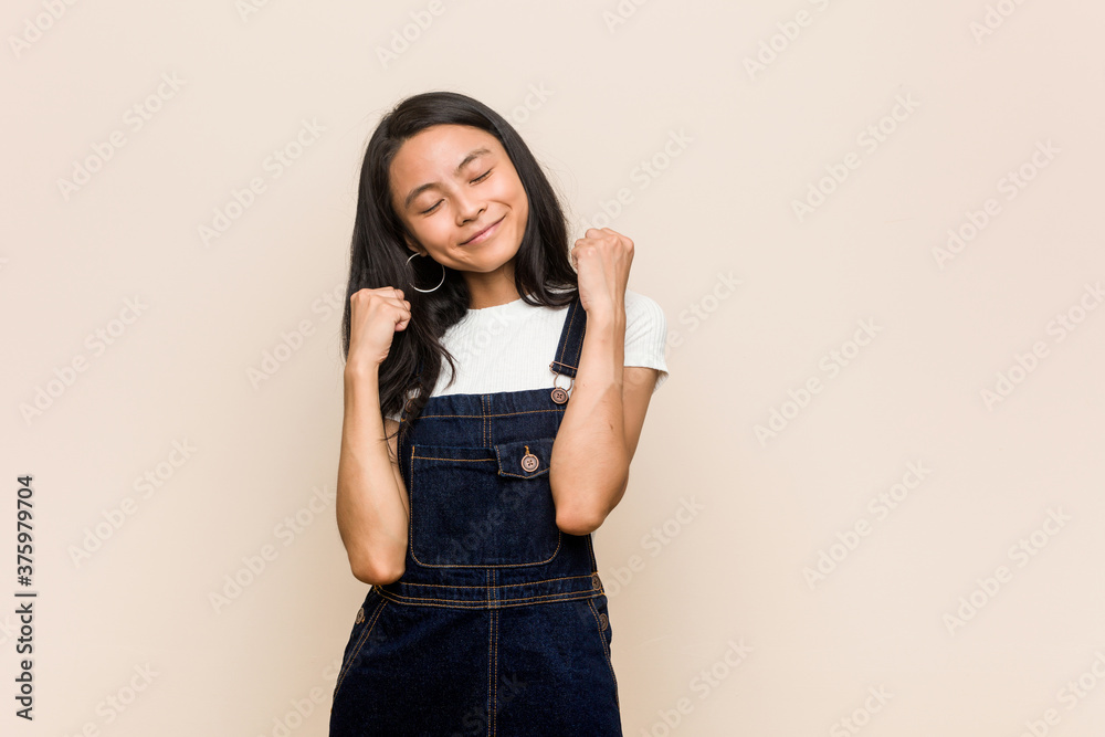 Φωτογραφία Young cute chinese teenager Young blonde woman wearing a coat against a pink background raising fist, feeling happy and successful