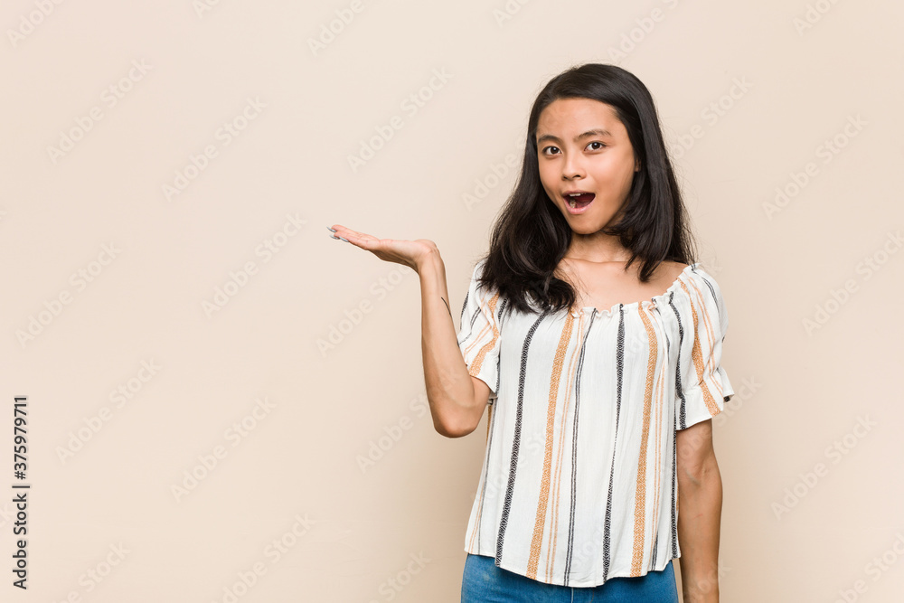 Young cute chinese teenager Young blonde woman wearing a coat against a pink background impressed holding copy space on palm. Young cute chinese teenager Young blonde woman wearing a coat against a pink background impressed holding copy space on palm.