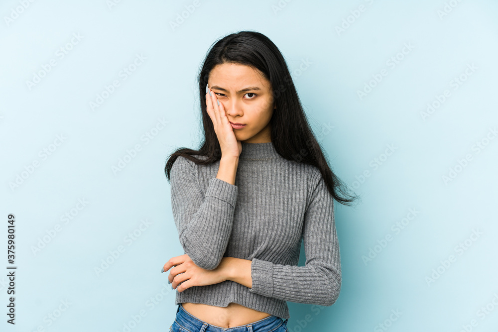 Young chinese woman isolated on a blue background who is bored, fatigued and need a relax day. Young chinese woman isolated on a blue background who is bored, fatigued and need a relax day.