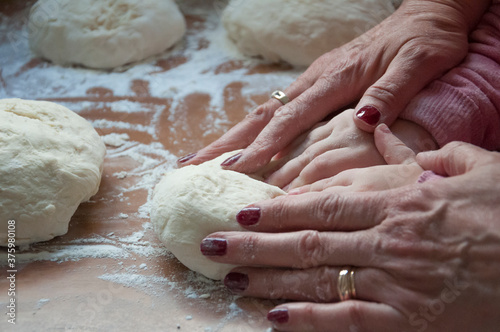 Hands of a little girl kneading dough for pizza with her mother