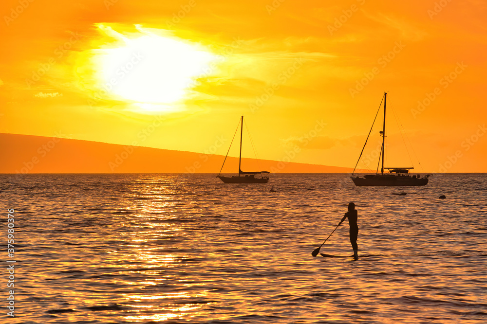 Stand up paddle boarder silhouetted at sunset looking ou to the sunset.