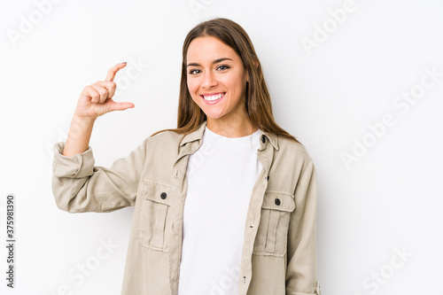 Young caucasian woman  isolated holding something little with forefingers, smiling and confident.