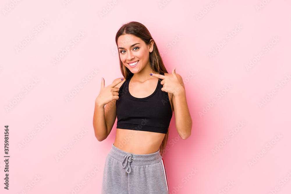 Young caucasian fitness woman posing in a pink background smiles, pointing fingers at mouth.
