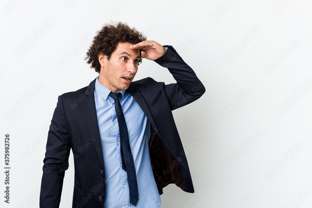 Young business curly man against white background looking far away keeping hand on forehead. Young business curly man against white background looking far away keeping hand on forehead.