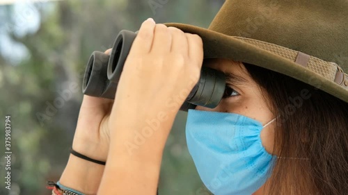traveling tourist girl with bionoculars in a medical face mask. Concept of Corona virus impact on a travel industry & tourism. photo