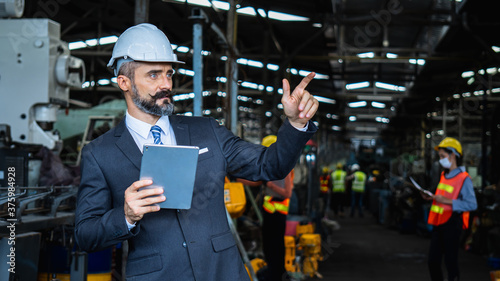 industrial manager in suit and wearing white protect helmet, check and control worker with tablet in industry, inspection and management in factory by technology concept