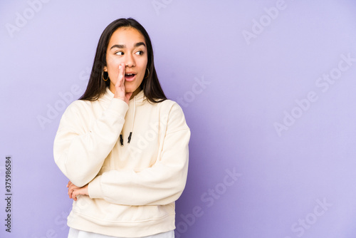 Young woman isolated on a purple background is saying a secret hot braking news and looking aside