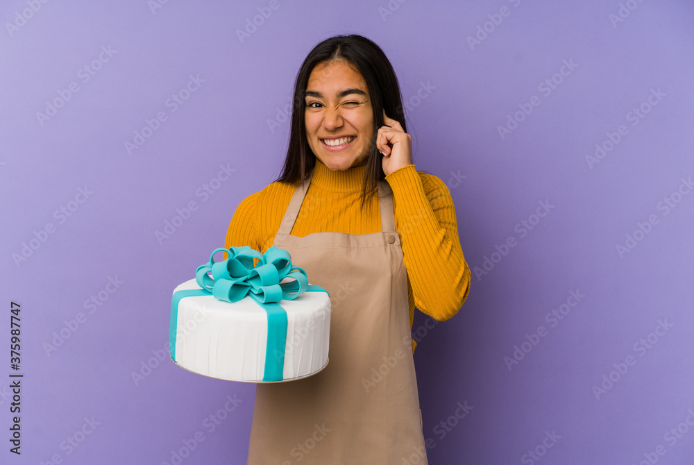 Young asian woman holding a cake isolated covering ears with hands. Young asian woman holding a cake isolated covering ears with hands.