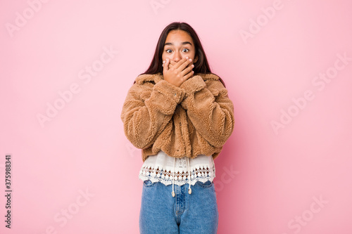 Young mixed race indian woman wearing a short sheepskin coatshocked covering mouth with hands.