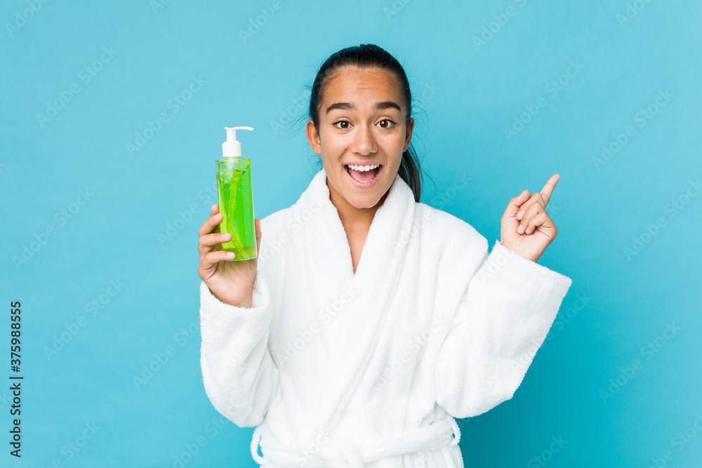 Young mixed race indian holding an aloe vera bottle smiling cheerfully pointing with forefinger away. Young mixed race indian holding an aloe vera bottle smiling cheerfully pointing with forefinger away.