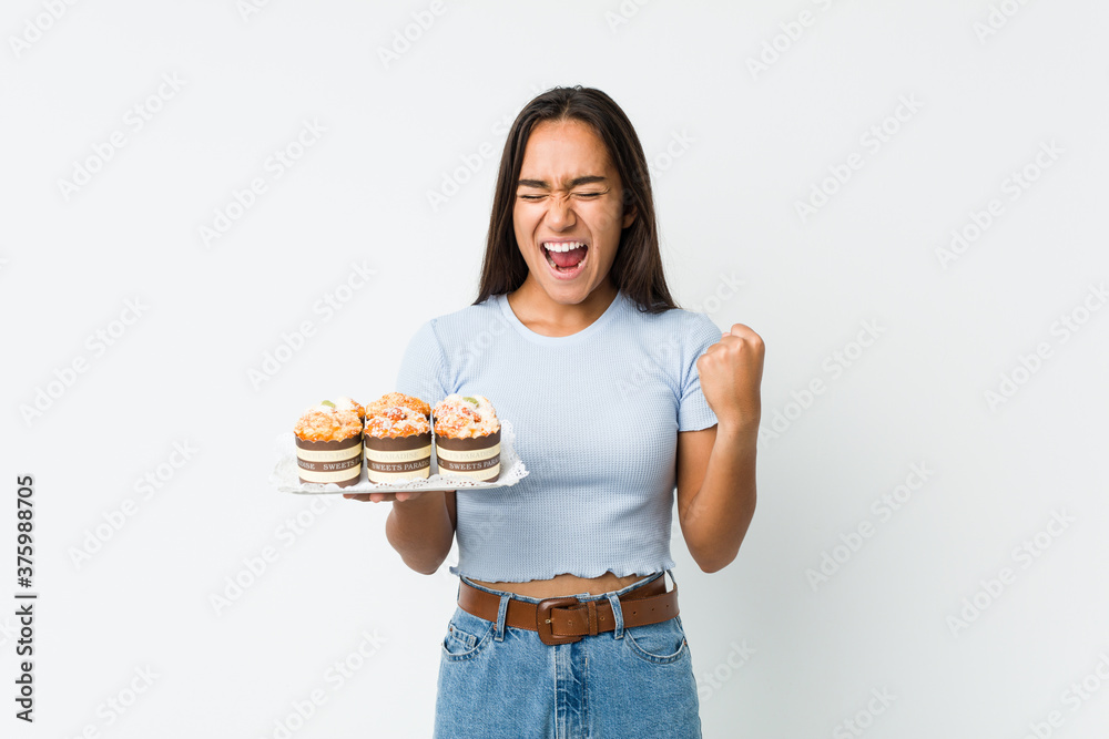 Young mixed race indian holding a sweet cakes cheering carefree and excited. Victory concept. Young mixed race indian holding a sweet cakes cheering carefree and excited. Victory concept.