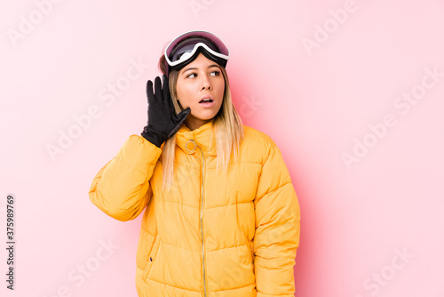 Young caucasian woman wearing a ski clothes in a pink background trying to listening a gossip. © Asier