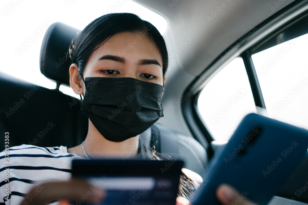 Young asian woman sitting at backseat of car and using mobile and holding credit card in hands.