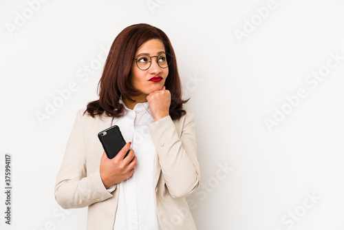 Middle age latin woman holding a mobile phone isolated looking sideways with doubtful and skeptical expression.