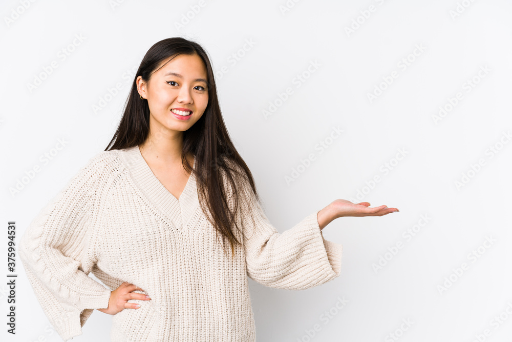 Young chinese woman isolated showing a copy space on a palm and holding another hand on waist. Young chinese woman isolated showing a copy space on a palm and holding another hand on waist.