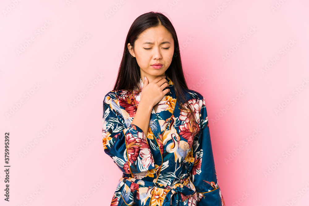 Young chinese woman wearing a kimono pajama isolated suffers pain in throat due a virus or infection. Young chinese woman wearing a kimono pajama isolated suffers pain in throat due a virus or infection.