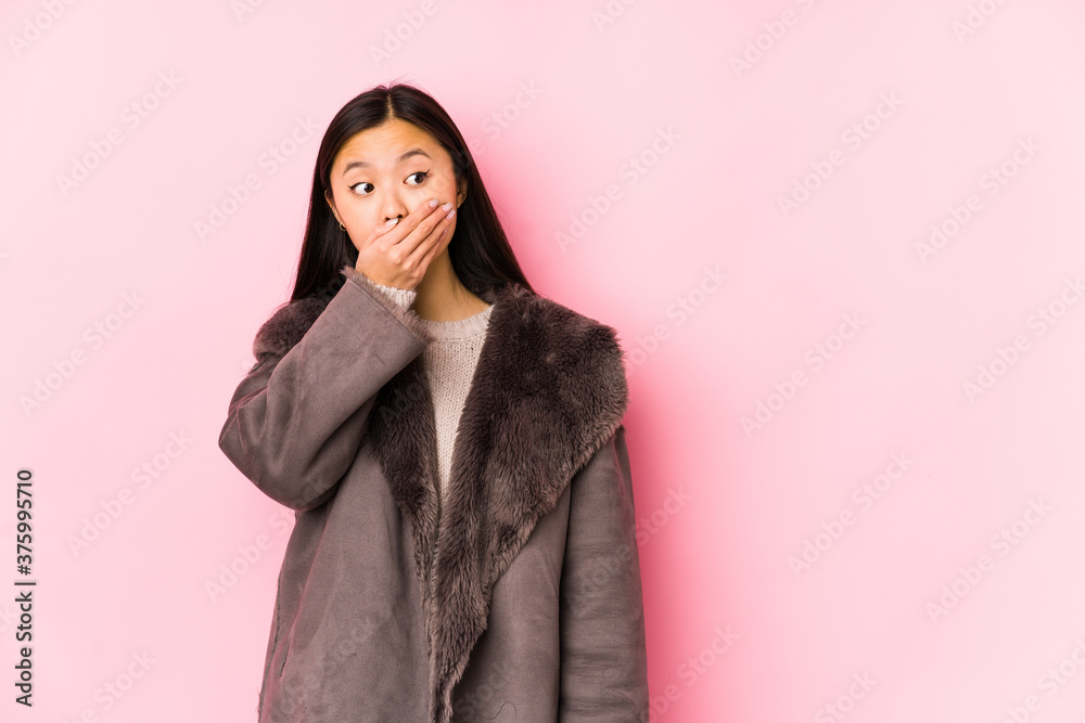 Young chinese woman wearing a coat isolated thoughtful looking to a copy space covering mouth with hand. Young chinese woman wearing a coat isolated thoughtful looking to a copy space covering mouth with hand.
