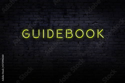 Billede på lærred Night view of neon sign on brick wall with inscription guidebook
