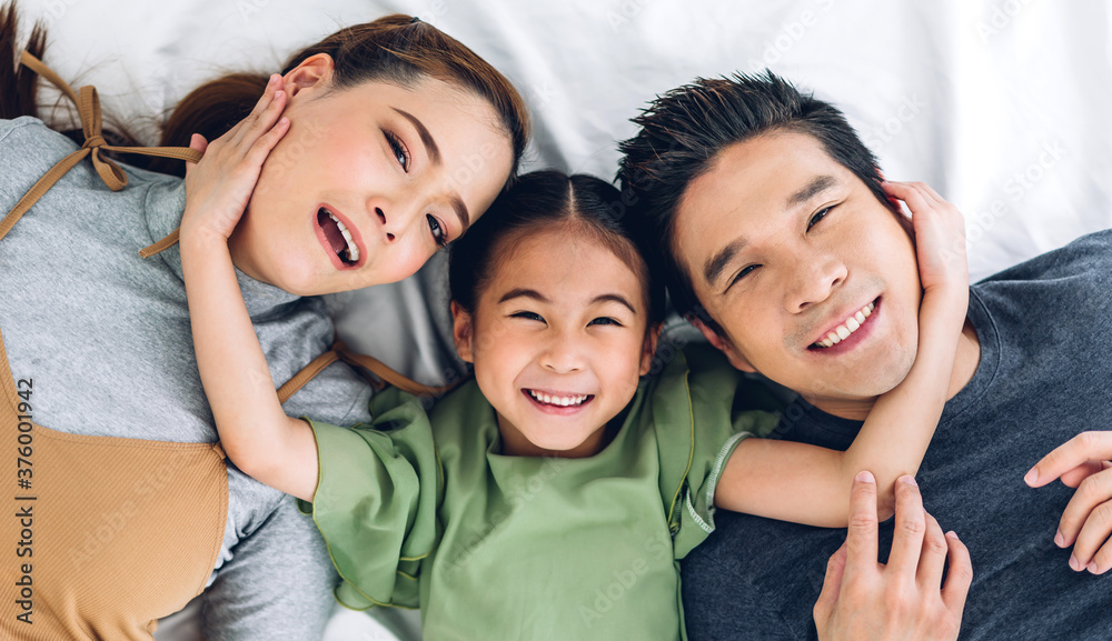 Top view of portrait enjoy happy smiling love asian family father and mother with young parents little asian girl looking at camera in moments good time lying on the floor at home