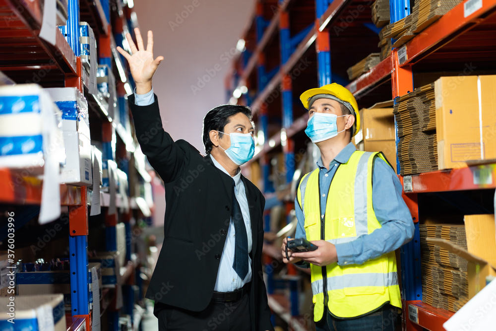 Management visits and inspects the work request for employees in the warehouse. Worker man wearing face mask prevent covid-19 virus and protective hard hat. Management visits and inspects the work request for employees in the warehouse. Worker man wearing face mask prevent covid-19 virus and protective hard hat.
