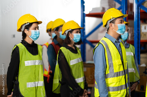 Warehouse managers and worker wearing face mask prevent covid-19 virus and protective hard hat and working together in warehouse workplace. Professional engineering team.