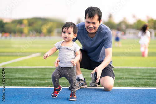 A cute little baby boy is learning to walk for his first step and daddy help to support the child with fully happiness moment, concept of baby growth and development and role of parent in family life