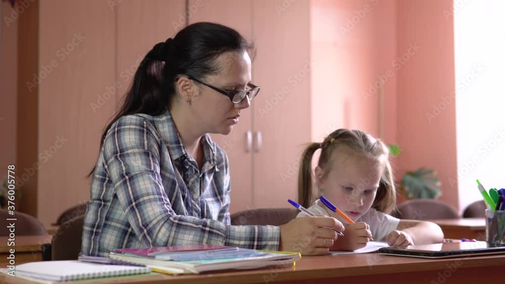 Little beautiful girl is studies with the teacher in the school class. Draws in a notebook with a pen. Preschool education.4k Little beautiful girl is studies with the teacher in the school class. Draws in a notebook with a pen. Preschool education.4k