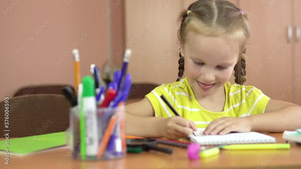 Little cute girl sits at a desk in the classroom. Draws in a notebook with a felt-tip pen. 4k Little cute girl sits at a desk in the classroom. Draws in a notebook with a felt-tip pen. 4k