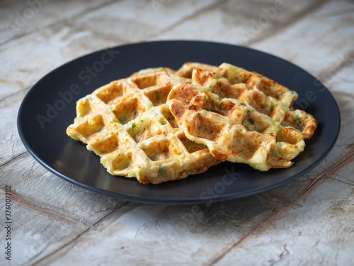 Zucchini waffles with the addition of greens and cheese on a close plate standing on a wooden decorative table