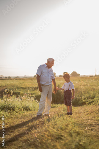 Happy senior man Grandfather with cute little boy grandson playing in field.