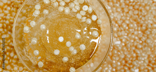 Glass jar with paste for sugaring close-up on the background of scattered pellets. Banner.View from the top photo