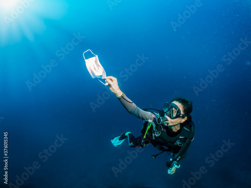 Photo Concept of sea pollution with a scuba diver who picks up a used face mask underw