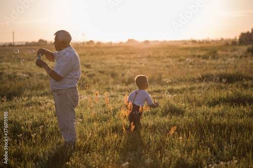 Happy senior man Grandfather with cute little boy grandson playing in field. Happy child with Grandfather playing outdoors