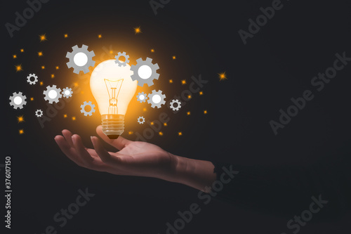 Hand holding illuminated light bulb and cog, idea and imagination, creative, innovation inspiration concept.